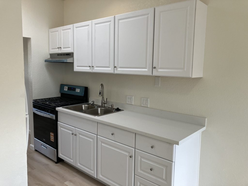 Kitchen after — white cabinets, new counters, sink, and range